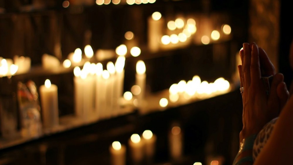 hands in prayer in front of lit candles 